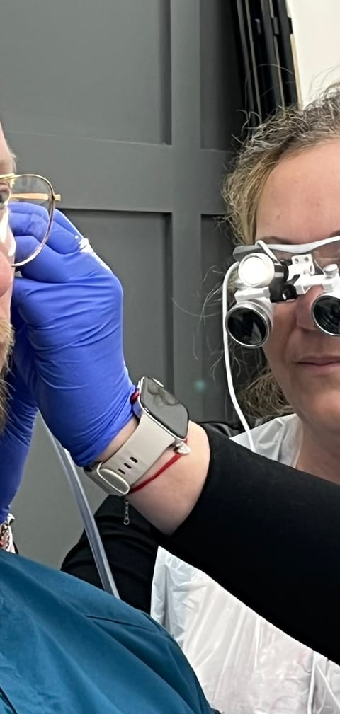Ear wax removal by microsuction in progress, the practitioner viewing the ear canal through magnifying loupes